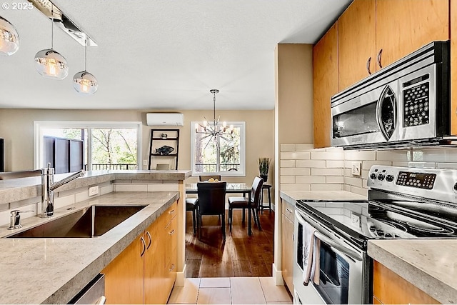 kitchen with sink, a wall mounted air conditioner, hanging light fixtures, stainless steel appliances, and decorative backsplash