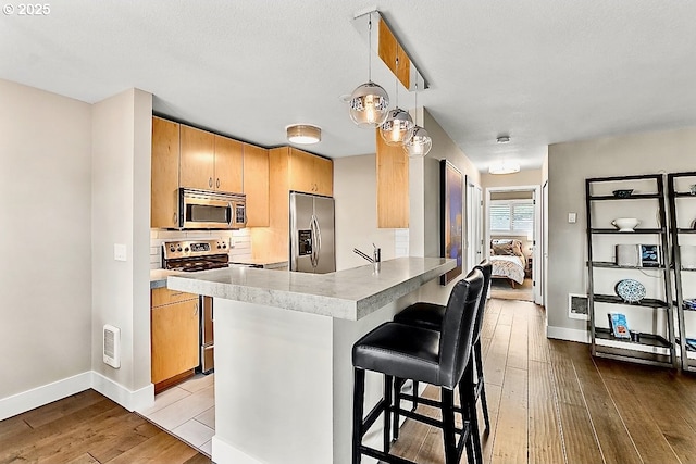 kitchen featuring a breakfast bar area, hanging light fixtures, stainless steel appliances, kitchen peninsula, and light wood-type flooring