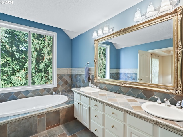 bathroom with vanity, lofted ceiling, a textured ceiling, and tiled bath