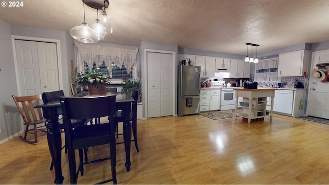 kitchen with white appliances, white cabinets, a textured ceiling, extractor fan, and hanging light fixtures