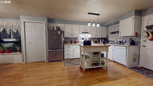 kitchen with stainless steel refrigerator, white dishwasher, pendant lighting, white cabinets, and light hardwood / wood-style flooring