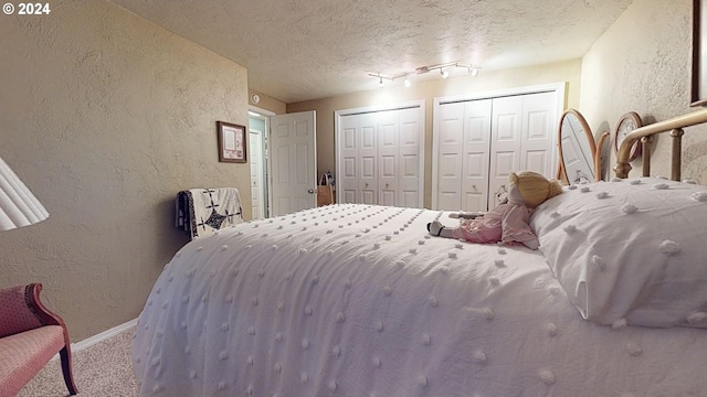 bedroom with carpet flooring, a textured ceiling, and two closets