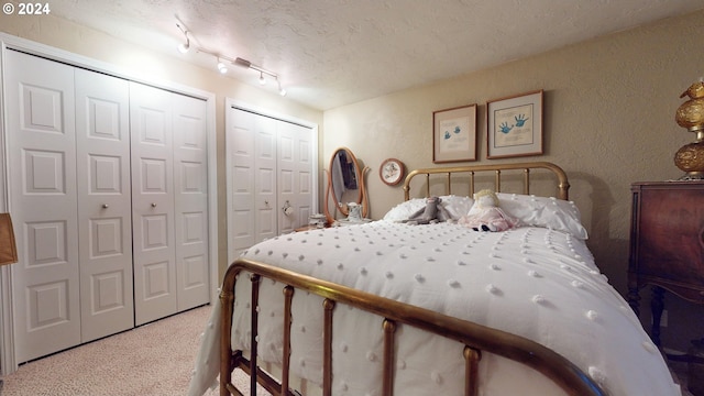 bedroom featuring multiple closets, carpet, a textured ceiling, a textured wall, and track lighting