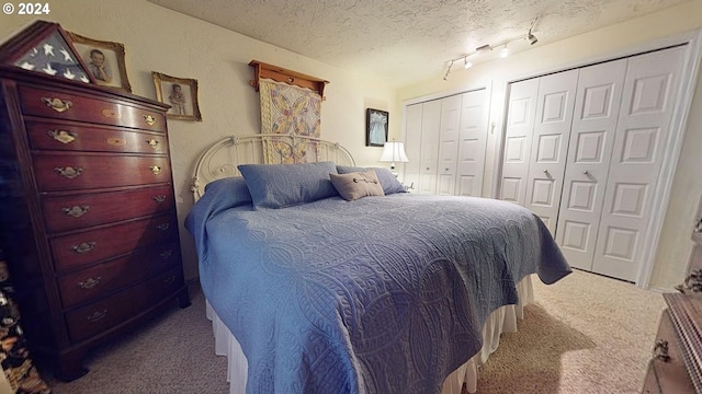 carpeted bedroom with a textured ceiling, track lighting, and two closets