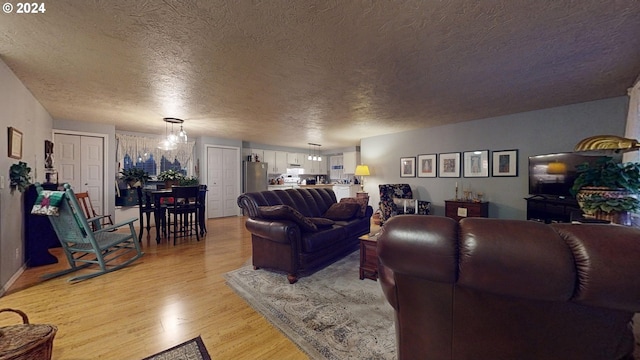 living room featuring an inviting chandelier, a textured ceiling, and light hardwood / wood-style flooring