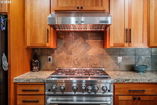 kitchen with tasteful backsplash, light stone countertops, stainless steel range, and range hood