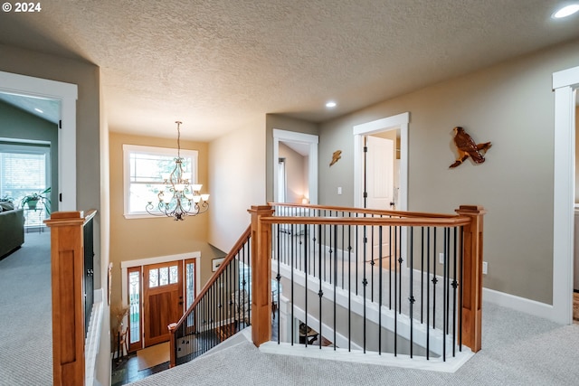 hall with carpet flooring, a textured ceiling, a wealth of natural light, and a notable chandelier