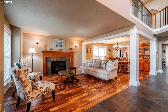 living room with dark hardwood / wood-style flooring, a tiled fireplace, a textured ceiling, and decorative columns