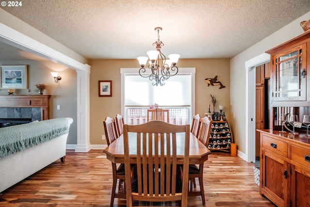 dining space with a tiled fireplace, light hardwood / wood-style flooring, a chandelier, and a textured ceiling