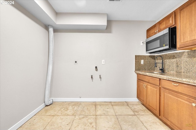 kitchen featuring light tile patterned flooring, sink, light stone counters, and decorative backsplash