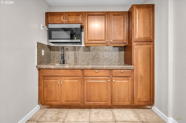 kitchen with tasteful backsplash, sink, light tile patterned floors, and stone countertops