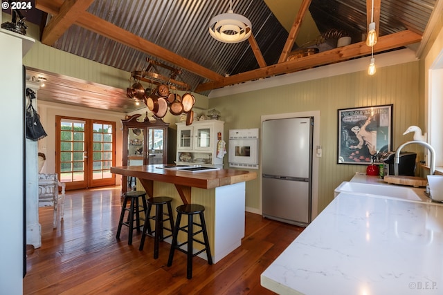 kitchen featuring french doors, stainless steel fridge, white cabinetry, a kitchen bar, and beam ceiling