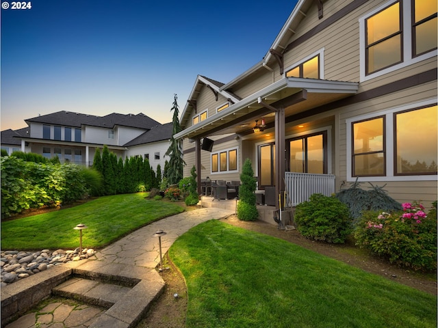 property exterior at dusk with ceiling fan, a lawn, and a patio