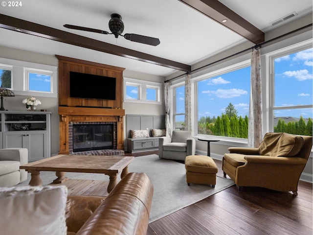 living room featuring a brick fireplace, ceiling fan, beamed ceiling, and dark hardwood / wood-style flooring