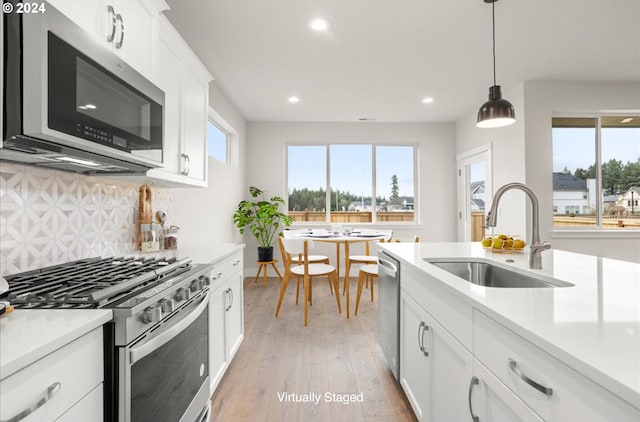 kitchen featuring sink, hanging light fixtures, light hardwood / wood-style flooring, white cabinets, and appliances with stainless steel finishes