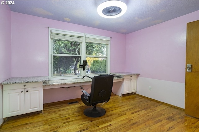 office space featuring built in desk, a textured ceiling, and light hardwood / wood-style flooring