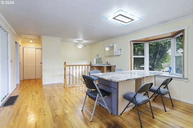 kitchen with light hardwood / wood-style floors, a textured ceiling, a kitchen bar, and ornamental molding