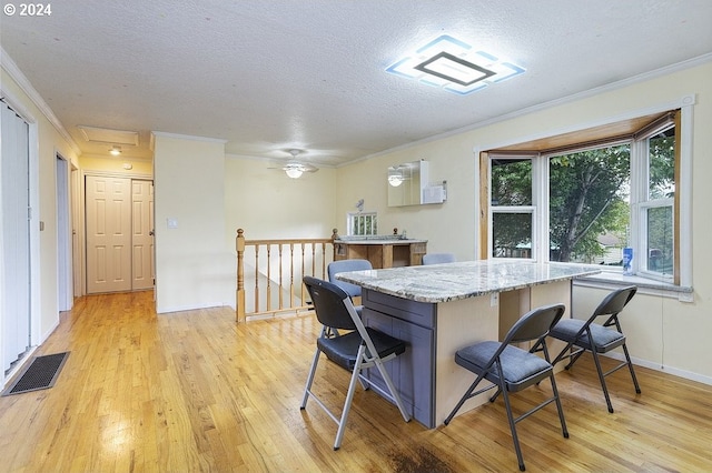kitchen with light wood-style floors, ornamental molding, a kitchen bar, and a textured ceiling