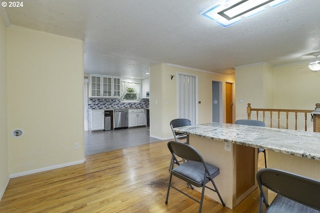 kitchen featuring decorative backsplash, ornamental molding, a breakfast bar, stainless steel dishwasher, and light hardwood / wood-style floors