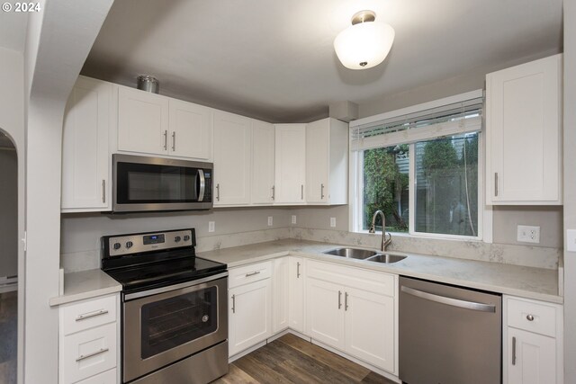 kitchen featuring sink, appliances with stainless steel finishes, dark wood-type flooring, light stone countertops, and white cabinetry