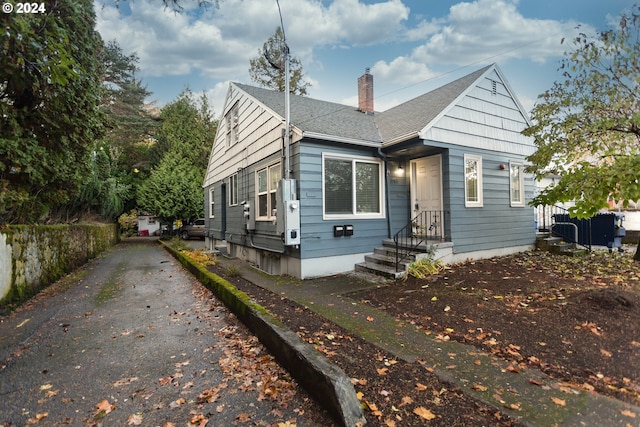 bungalow-style home with roof with shingles, driveway, and a chimney