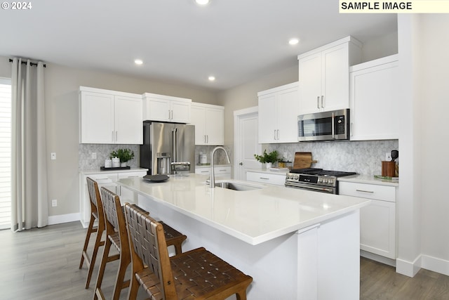 kitchen featuring a breakfast bar, stainless steel appliances, a kitchen island with sink, sink, and white cabinets