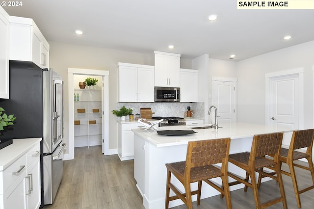 kitchen featuring light wood-type flooring, stainless steel appliances, sink, a center island with sink, and white cabinets