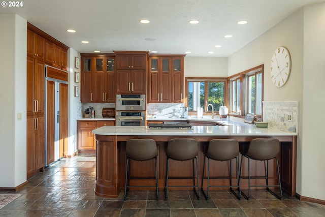 kitchen with paneled built in refrigerator, sink, kitchen peninsula, backsplash, and double oven