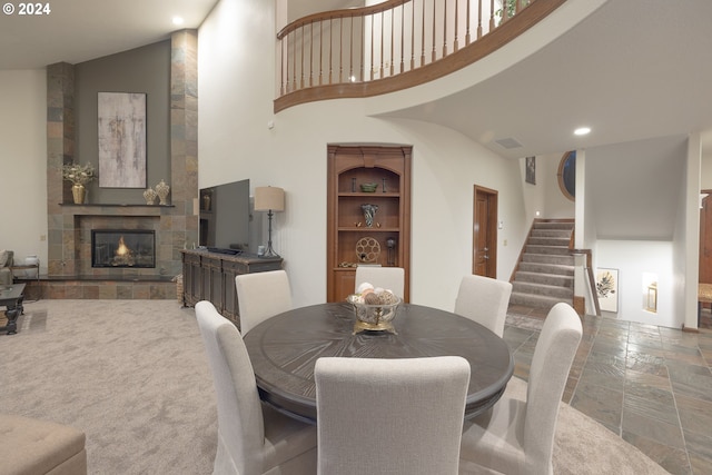 carpeted dining area with a towering ceiling and a tiled fireplace