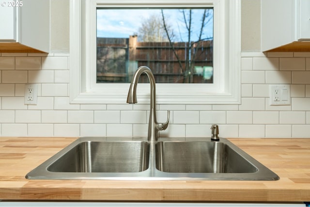 details featuring tasteful backsplash, white cabinetry, sink, and butcher block counters