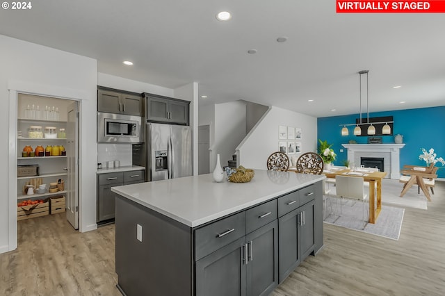 kitchen with stainless steel appliances, decorative light fixtures, light hardwood / wood-style flooring, a kitchen island, and gray cabinetry