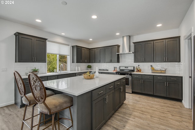 kitchen with dark brown cabinetry, light hardwood / wood-style flooring, a center island, wall chimney range hood, and stainless steel range