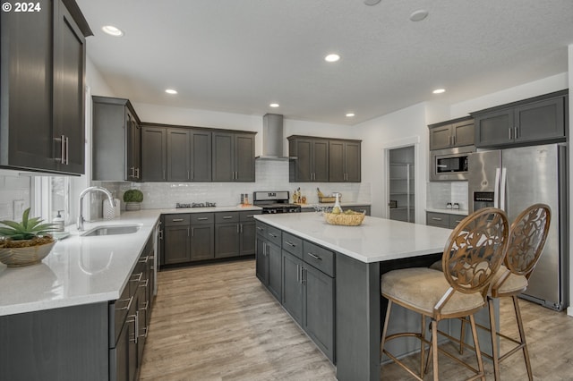 kitchen with light hardwood / wood-style floors, a center island, wall chimney exhaust hood, sink, and appliances with stainless steel finishes