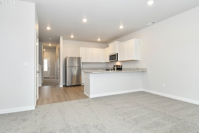 kitchen with white cabinets, light colored carpet, light stone counters, kitchen peninsula, and stainless steel appliances