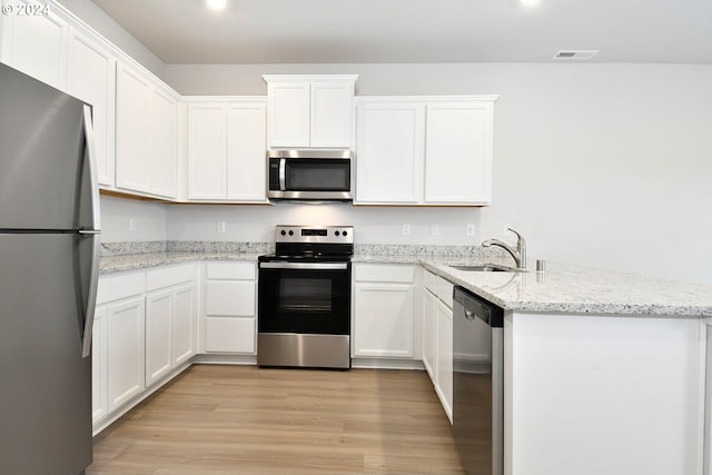 kitchen with light stone countertops, light wood-type flooring, stainless steel appliances, sink, and white cabinetry