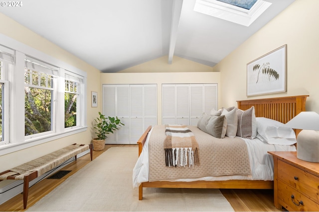 bedroom with vaulted ceiling with skylight, multiple closets, and light hardwood / wood-style flooring