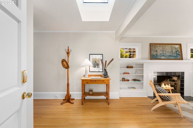 sitting room featuring a skylight, a tile fireplace, hardwood / wood-style flooring, and ornamental molding