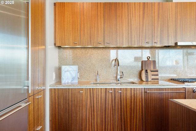 kitchen with gas stovetop, brown cabinetry, a sink, and built in fridge