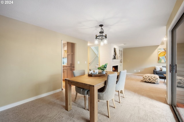 dining area with a fireplace, an inviting chandelier, and light colored carpet