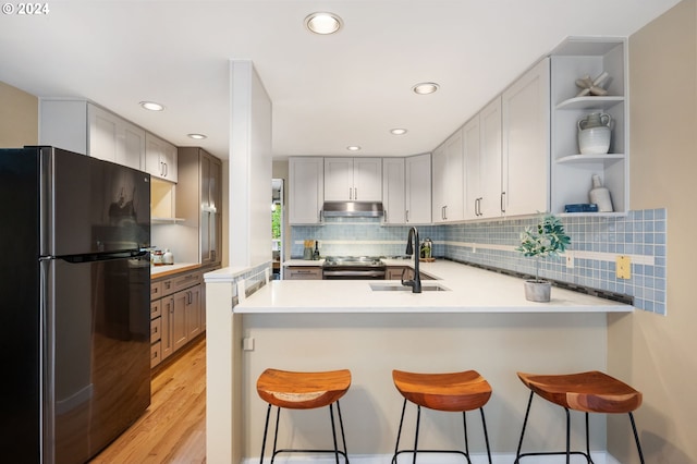 kitchen with sink, kitchen peninsula, a kitchen breakfast bar, light hardwood / wood-style floors, and black refrigerator