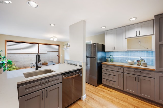 kitchen featuring tasteful backsplash, light wood-type flooring, sink, gray cabinetry, and stainless steel appliances