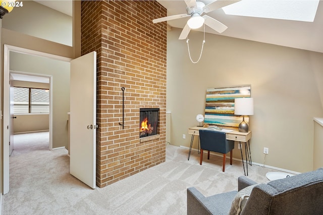 carpeted office featuring a skylight, a fireplace, high vaulted ceiling, and ceiling fan