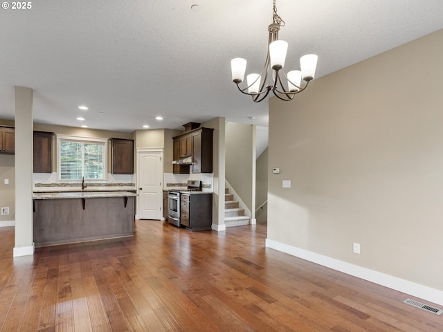 kitchen with stainless steel range with gas cooktop, dark brown cabinetry, under cabinet range hood, dark wood-style flooring, and baseboards