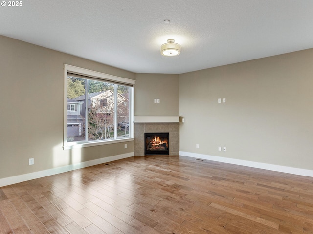unfurnished living room with a tile fireplace, baseboards, and wood finished floors