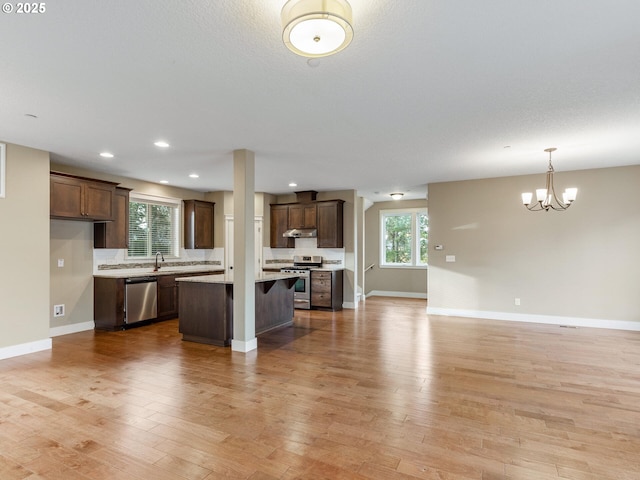 kitchen featuring an inviting chandelier, appliances with stainless steel finishes, under cabinet range hood, a sink, and open floor plan