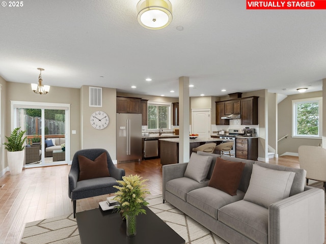 living room with light wood-style flooring, visible vents, recessed lighting, baseboards, and a notable chandelier