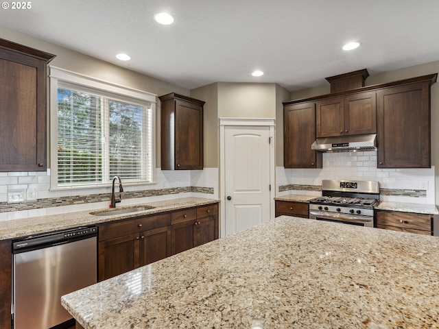 kitchen with tasteful backsplash, under cabinet range hood, light stone counters, a sink, and stainless steel appliances