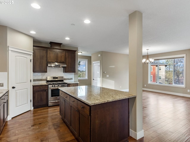 kitchen with tasteful backsplash, dark wood-style flooring, a notable chandelier, stainless steel gas range oven, and under cabinet range hood