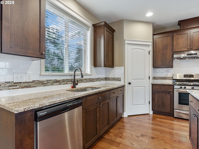 kitchen featuring tasteful backsplash, a sink, appliances with stainless steel finishes, under cabinet range hood, and light stone counters