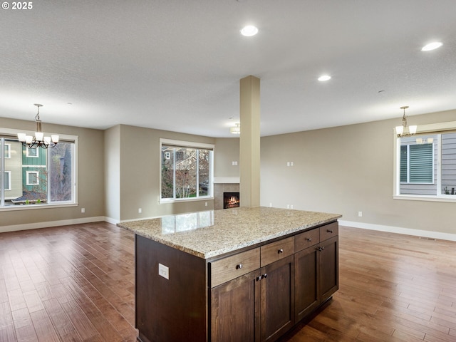 kitchen featuring dark wood finished floors, open floor plan, a notable chandelier, and a warm lit fireplace